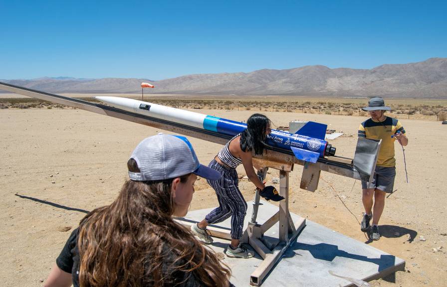 Three students with a small rocket in the desert.